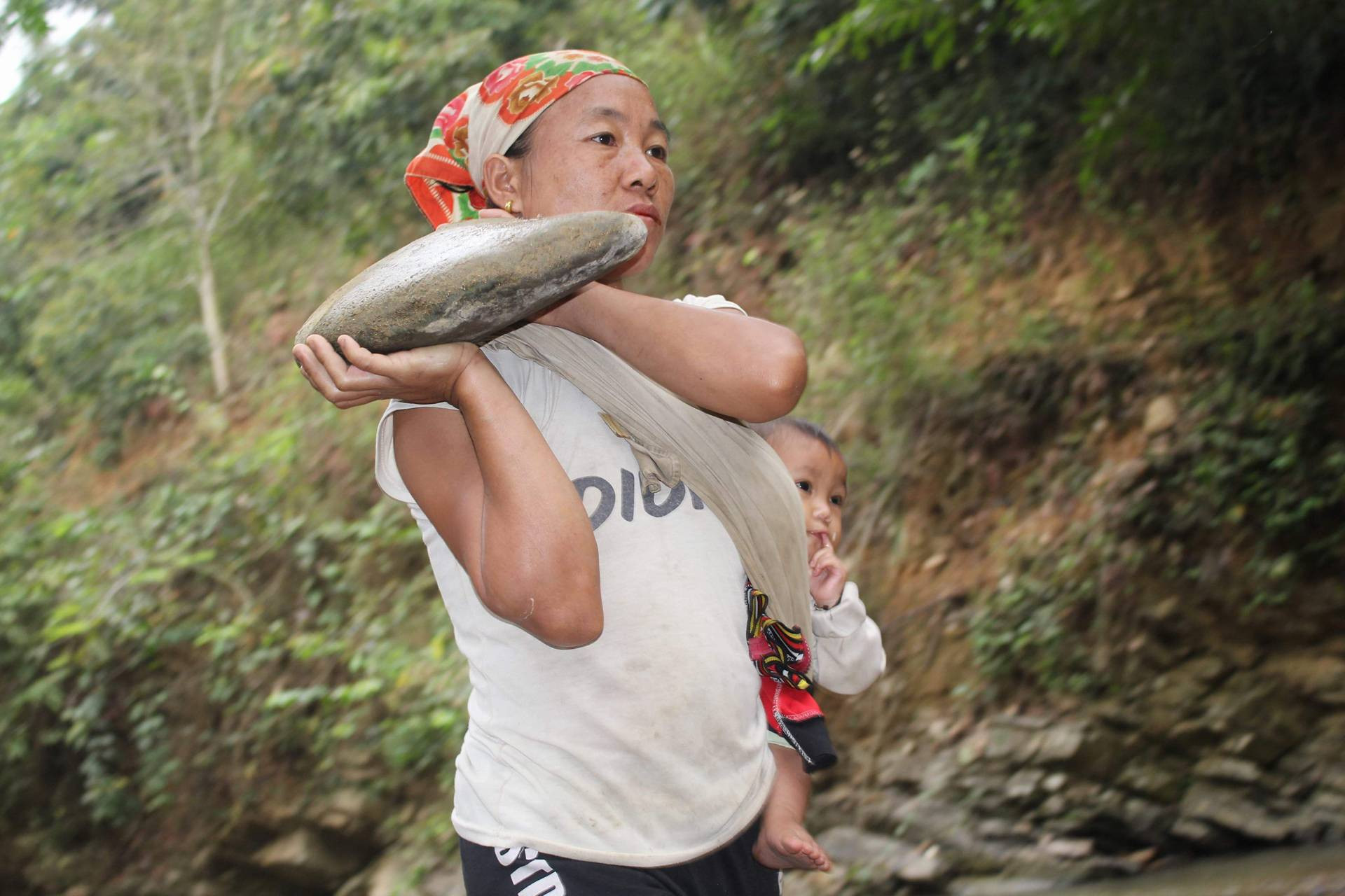 Một bà mẹ địu con vận chuyển đá xây cầu. Ảnh: Lữ Phú