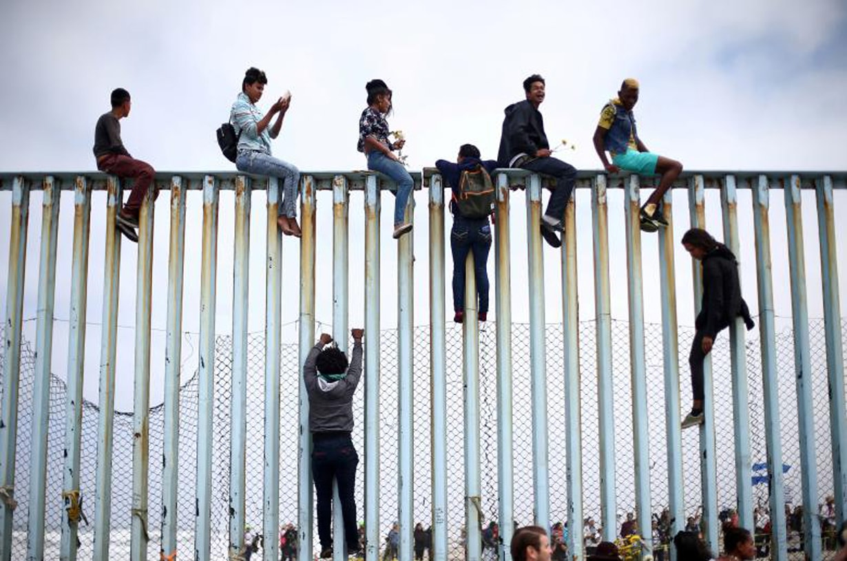 Người di cư từ Trung Mỹ trèo lên hàng rào biên giới giữa Mexico và Mỹ. Ảnh: Reuters