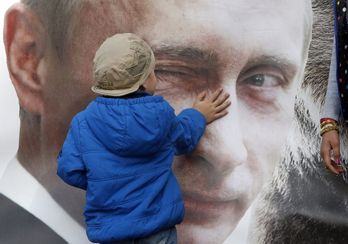 Một cậu bé đứng trước tấm áp phích in hình ông Putin ở St. Petersburg, Nga. Ảnh: AP