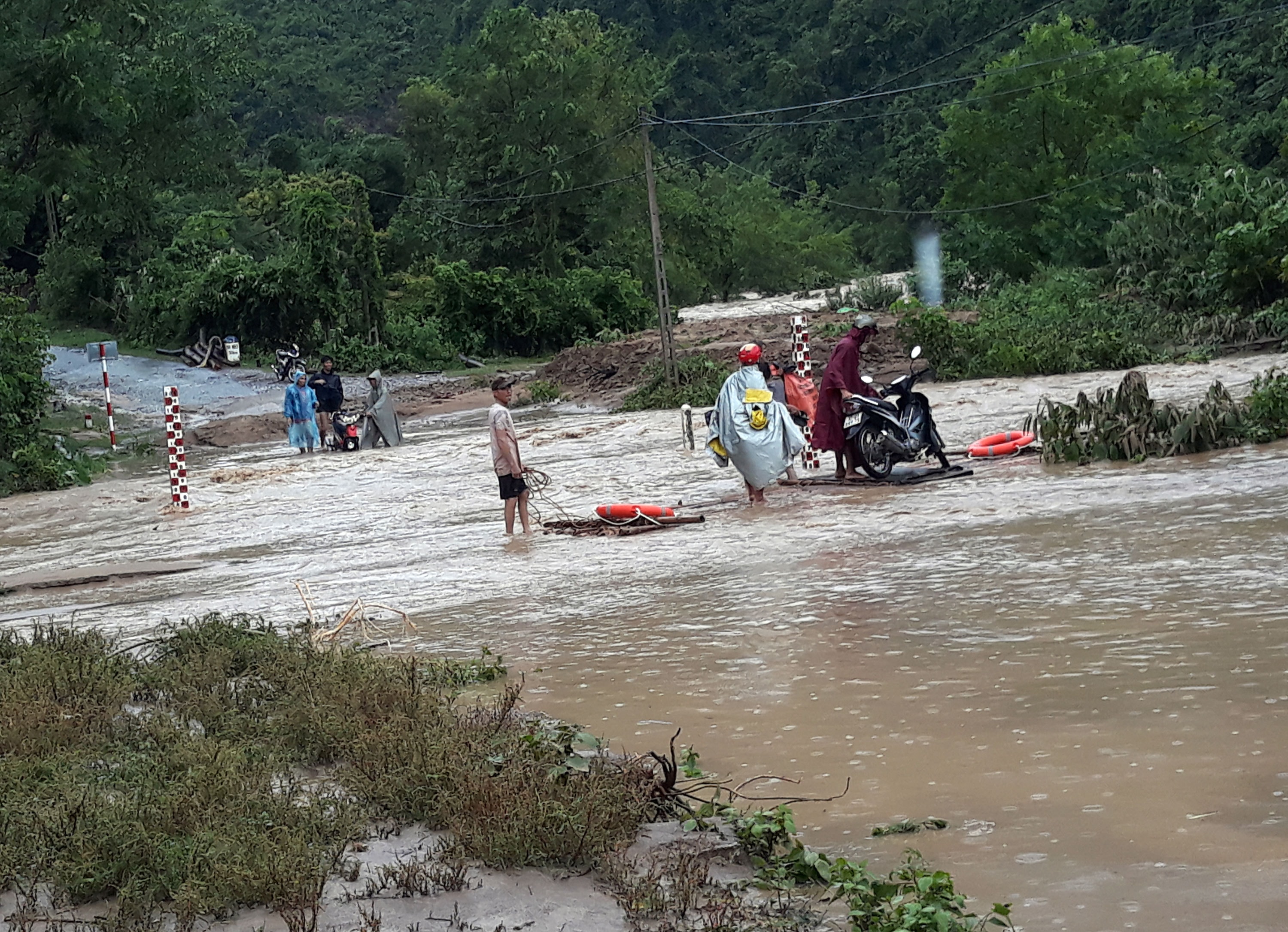 Việc người và xe cộ lưu thông qua đây cũng không đơn giản. Nhiều người chọn cách an toàn đi trên chiếc bè có dây neo và phao cứu hộ. Ảnh: Đào Thọ