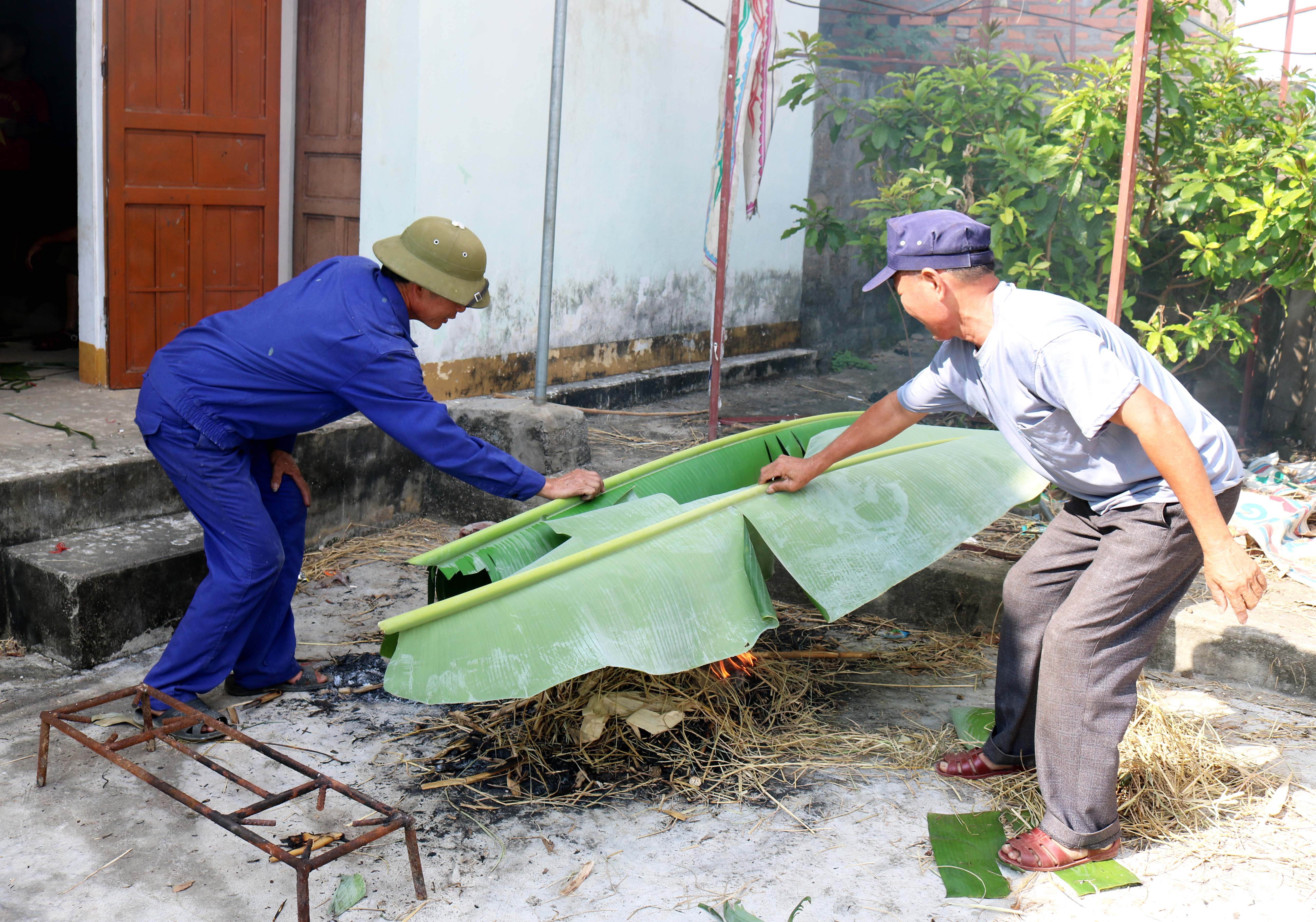 Mọi người tập trung về nhà văn hóa xóm, người được phân công hơ lá chuối, người chẻ dang, hầm đậu… chuẩn bị cho việc gói bánh chưng, Ảnh: Huy Thư