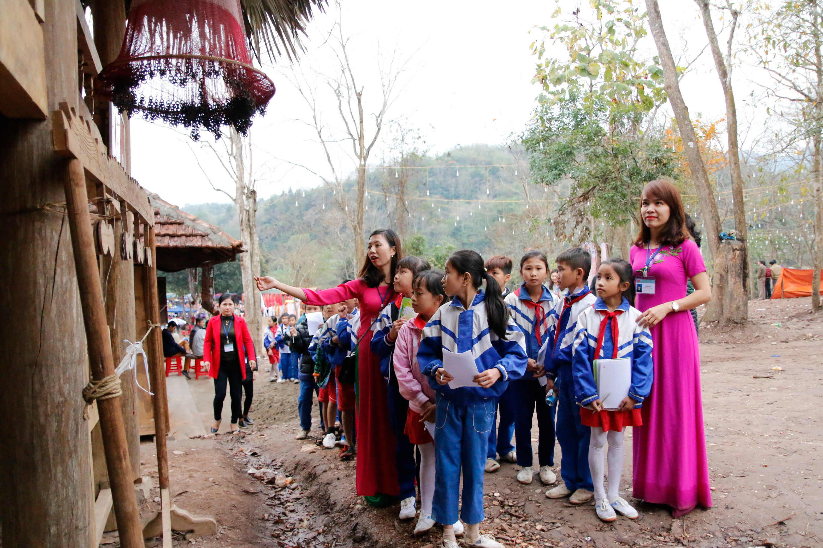Giáo viên giới thiệu cho các em học sinh về những vật dụng, nếp sinh hoạt của đồng bào tại mô hình làng văn hóa các dân tộc lễ hội đền Vạn- Cửa Rào. Ảnh Đặng Cường