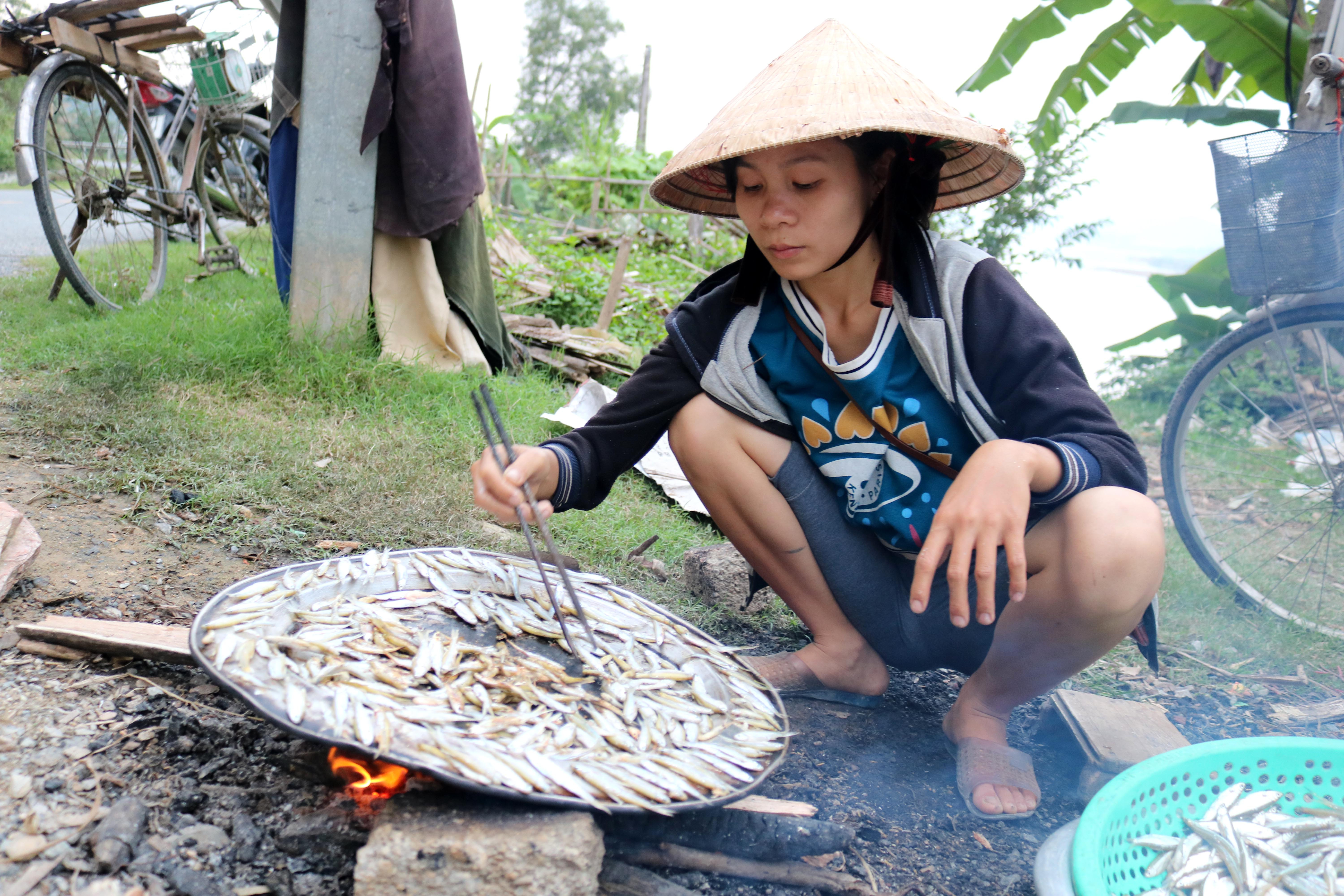 Một người phụ nữ quê tỉnh Quảng Bình lấy chồng về làng Hà Long đang ngồi nướng cá. Chị cho biết, hàng ngày chồng đi đánh cá còn vợ đem ra đây bán để kiếm gạo nuôi con.