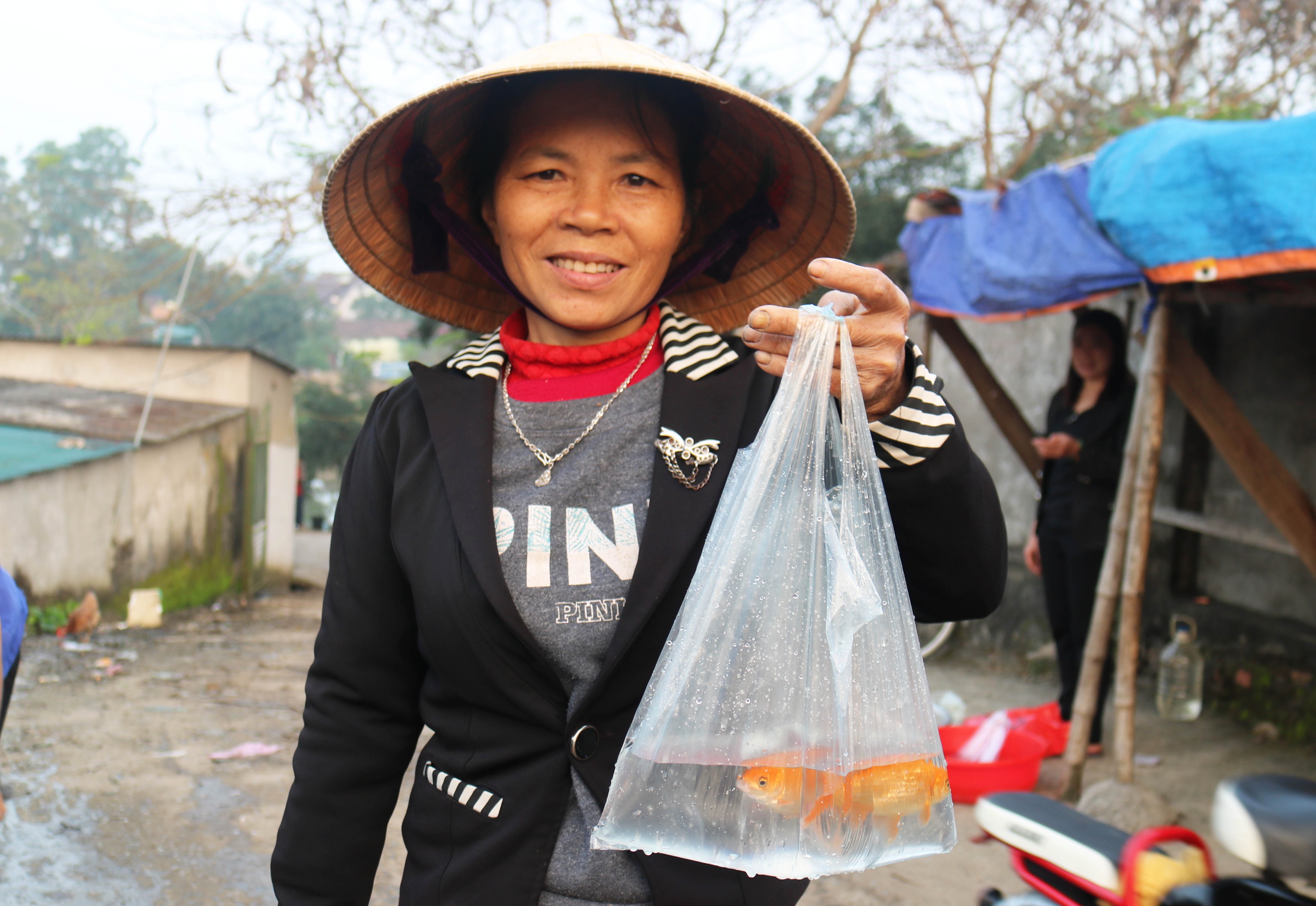 Một phụ nữ vui mừng vì đã mua được 3 con cá chép vàng ưng ý để về cúng ông Táo.