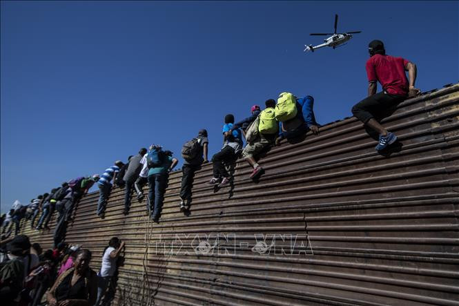 Người di cư trèo qua bức tường biên giới Mexico - Mỹ, gần cửa khẩu El Chaparral ở Tijuana, bang Baja California, Mexico, ngày 25/11/2018. Ảnh: AFP/TTXVN