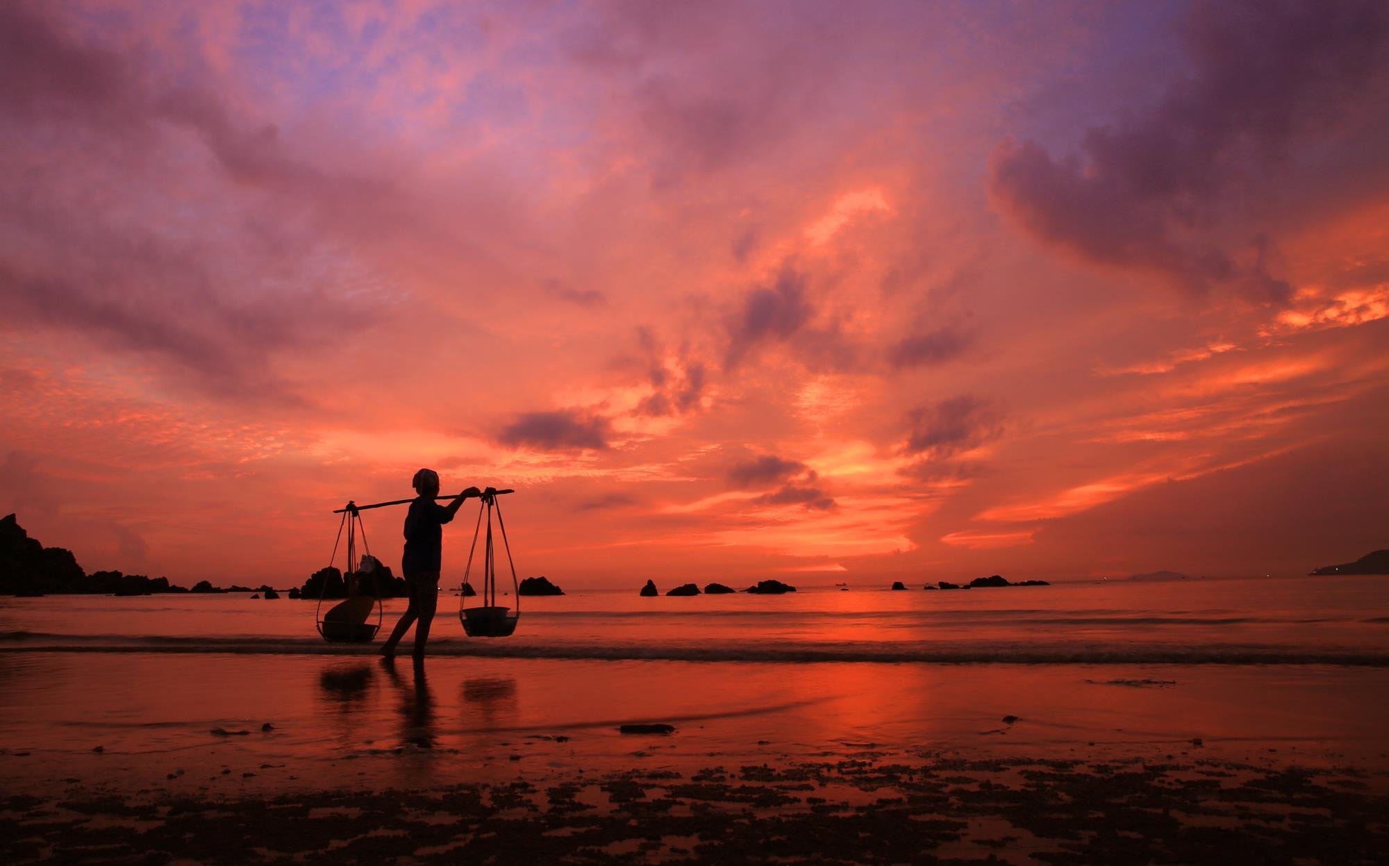 Người phụ nữ với quang gánh đang chờ chồng đi đánh bắt cá để kịp về mang đi ra chợ bán. Ảnh: Hồ Phương