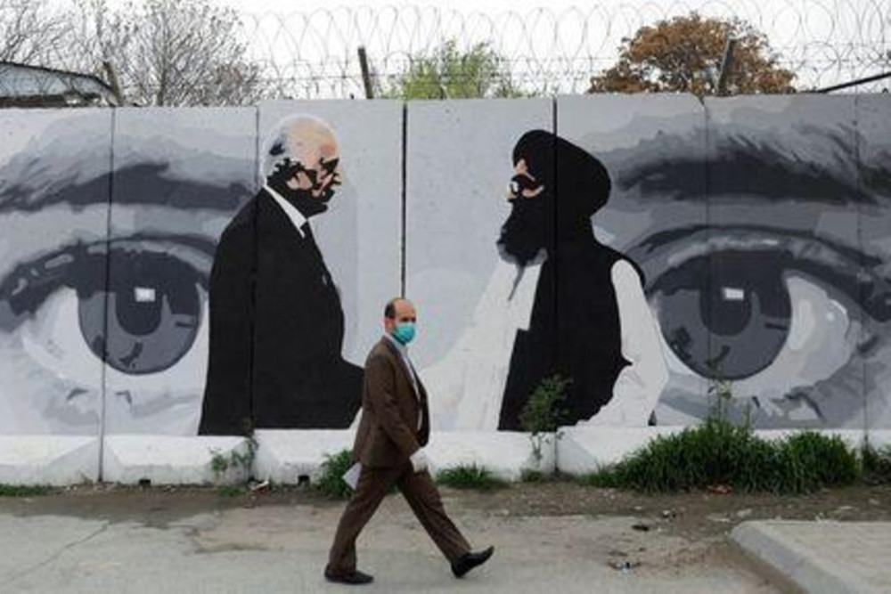 Một người đàn ông Afghanistan đeo khẩu trang đi ngang qua bức tường vẽ hình ảnh Đặc phái viên Mỹ về Afghanistan Zalmay Khalilzad và Người đứng đầu lực lượng Taliban Mullah Abdul Ghani Baradar, ở Kabul, Afghanistan ngày 13/4/2020. Ảnh: Reuters