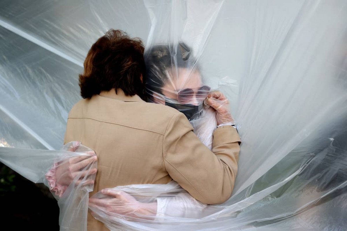 Olivia Grant ôm bà của mình, Mary Grace Sileo, qua một tấm vải nhựa ở Wantagh, New York ngày 24/5. Đây là lần đầu tiên họ gặp nhau kể từ khi đợt bùng phát dịch Covid-19 vào cuối tháng 2. Ảnh: Getty Images