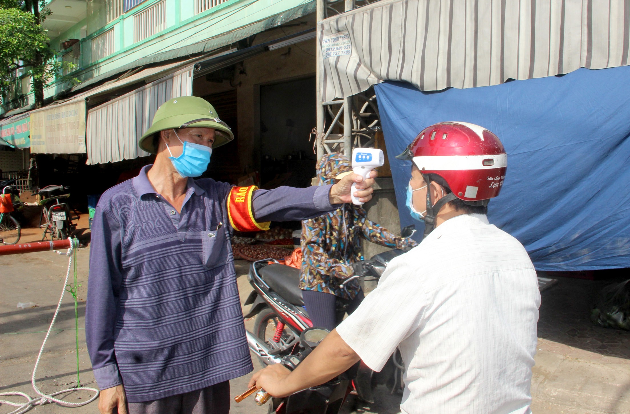 Lực lượng bảo vệ đo thân nhiệt cho người dân khi ra vào chợ. Ảnh: Quang An