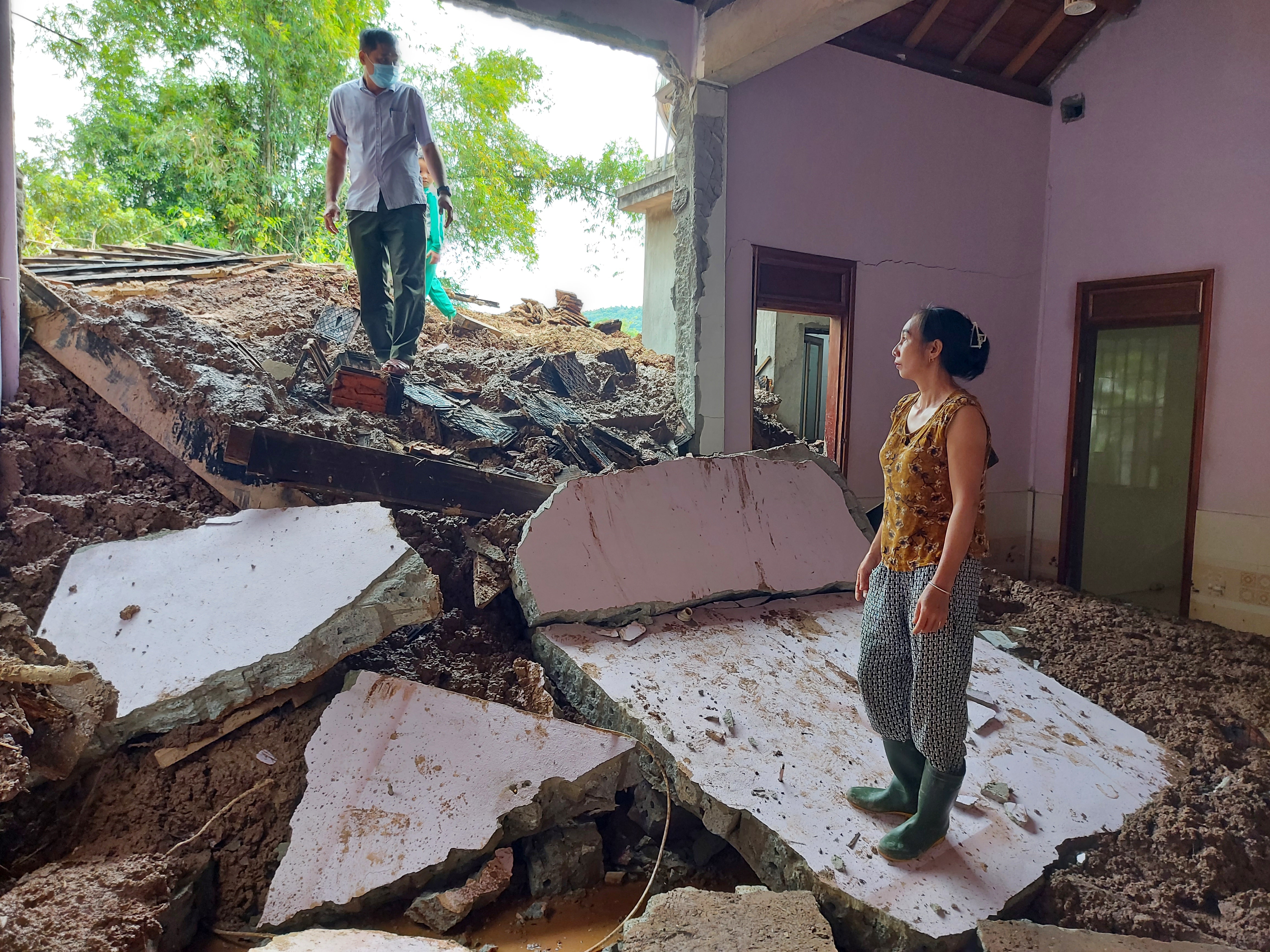 Ngôi nhà của ông Minh nằm sát tuyến đường đi xã Tam Hợp. Phía sau lưng là dãy núi cao sừng sững. Ông Minh kể rằng, từ xưa đến nay, khu vực này chưa hề xảy ra sạt lở núi. Tuy nhiên, khoảng 3h sáng 18/10, sau trận mưa kéo dài nhiều ngày, đất đá từ trên núi bắt đầu đổ xuống. “Đầu tiên là một tiếng nổ khá lớn, đánh thức vợ chồng tôi”, người đàn ông vẫn chưa hết bàng hoàng kể. Vợ chồng ông Minh lập tức hô hoán hàng xóm. Ban quản lý bản cũng ngay lập tức phát loa thông báo kêu gọi người dân đến hỗ trợ ông Minh và những hộ có nguy cơ bị sạt lở vận chuyển tài sản đến nơi an toàn.  Ảnh: Tiến Hùng