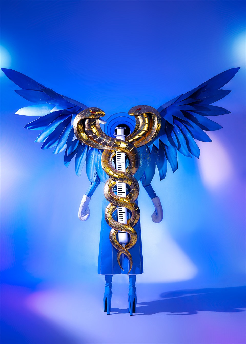 Phần cách điệu đôi rắn mạ vàng và điêu khắc thủ công quấn quanh ống tiêm vaccine cùng với đôi cánh sơn hiệu ứng ombre ánh kim, tạo nên hình ảnh biểu trưng của ngành y.