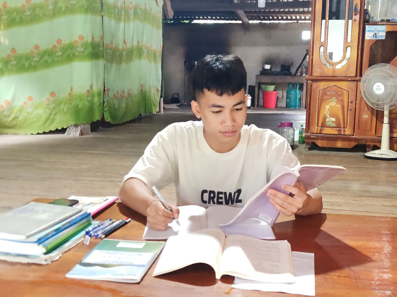 bna_ảnh. Trong ngôi nhà sàn nhỏ, ngoài giờ đi phụ hồ giúp bố Tuấn vẫn có thói quen ôn lại bài để củng cố kiến thức..jpg