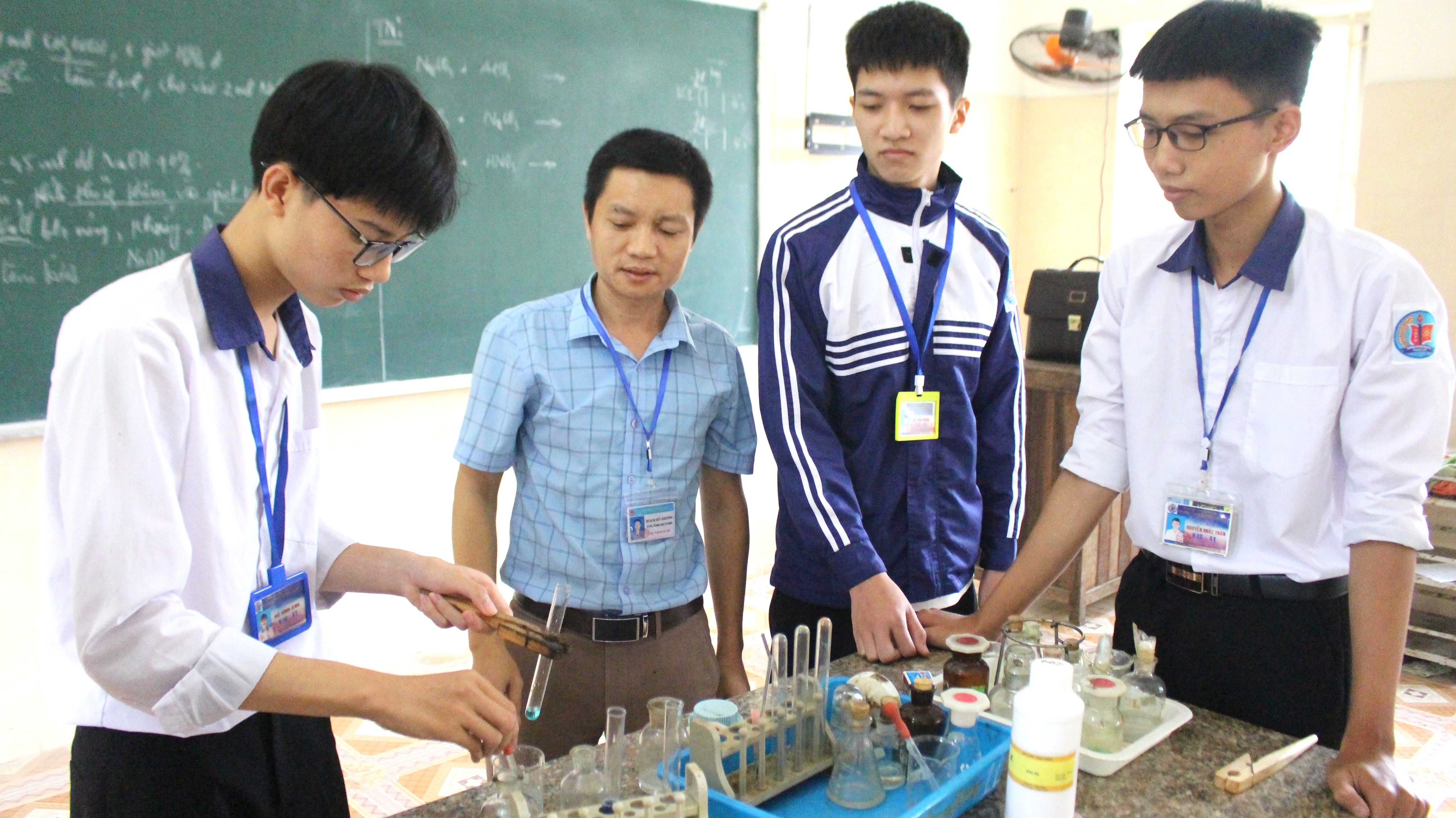 bna_Ánh và một số bạn trong đội tuyển bồi dưỡng học sinh giỏi được thầy giáo Quách Hữu Khương (áo xanh kẻ) hướng dẫn thực hành thí nghiệm.JPG