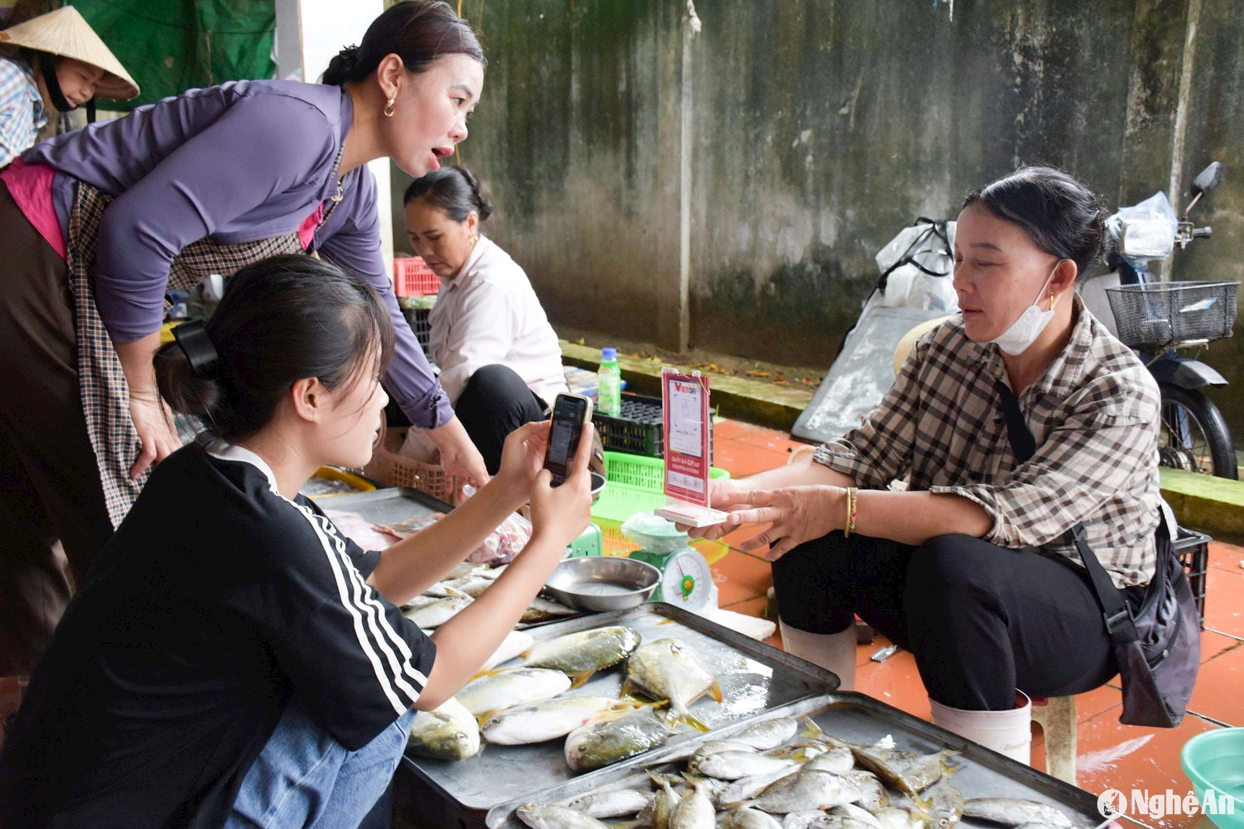 Người dân mua cá ở chợ Quỳnh Liên (Thị xã Hoàng Mai) thanh toán bằng mã QR. Chị Hồ Thị Minh, một người dân cho biết: “Thanh toán qua mã QR vừa nhanh, vừa tiện lại an toàn, sạch sẽ. Trước đây, mỗi lần đi chợ về, tiền thừa từ những tiểu thương phụ lại, tờ thì tanh mùi cá, tờ ám mùi thịt, tờ thì ướt nhẹp… rất bẩn”. Ảnh: Thanh Phúc