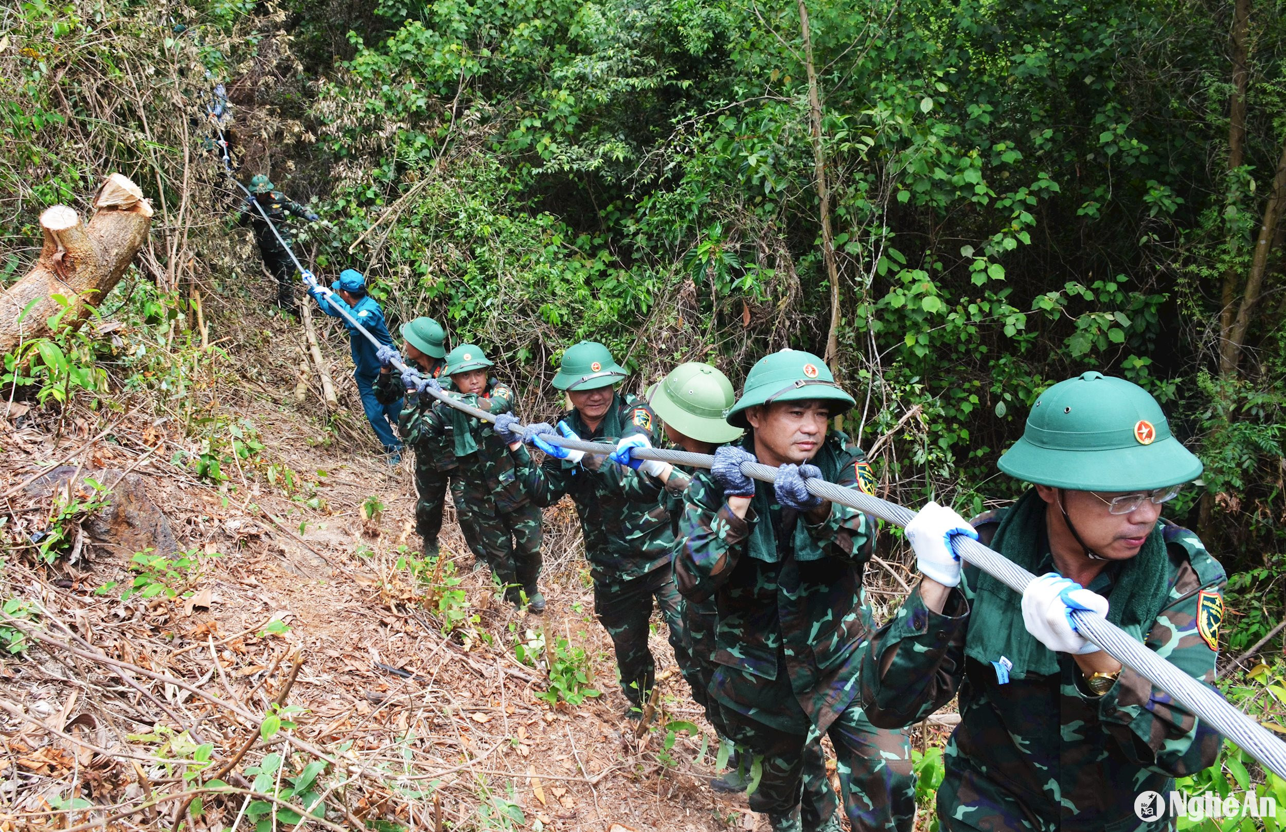 Cán bộ, chiến sĩ dân quân tự vệ, bộ đội thường trực chỗ trợ vận chuyển cuộn cáp điện, vật liệu, rải kéo dây tại khu vực khe Sâu, ở núi Thiên Nhẫn, xã Khánh Sơn, huyện Nam Đàn. Ảnh: Thành Chung