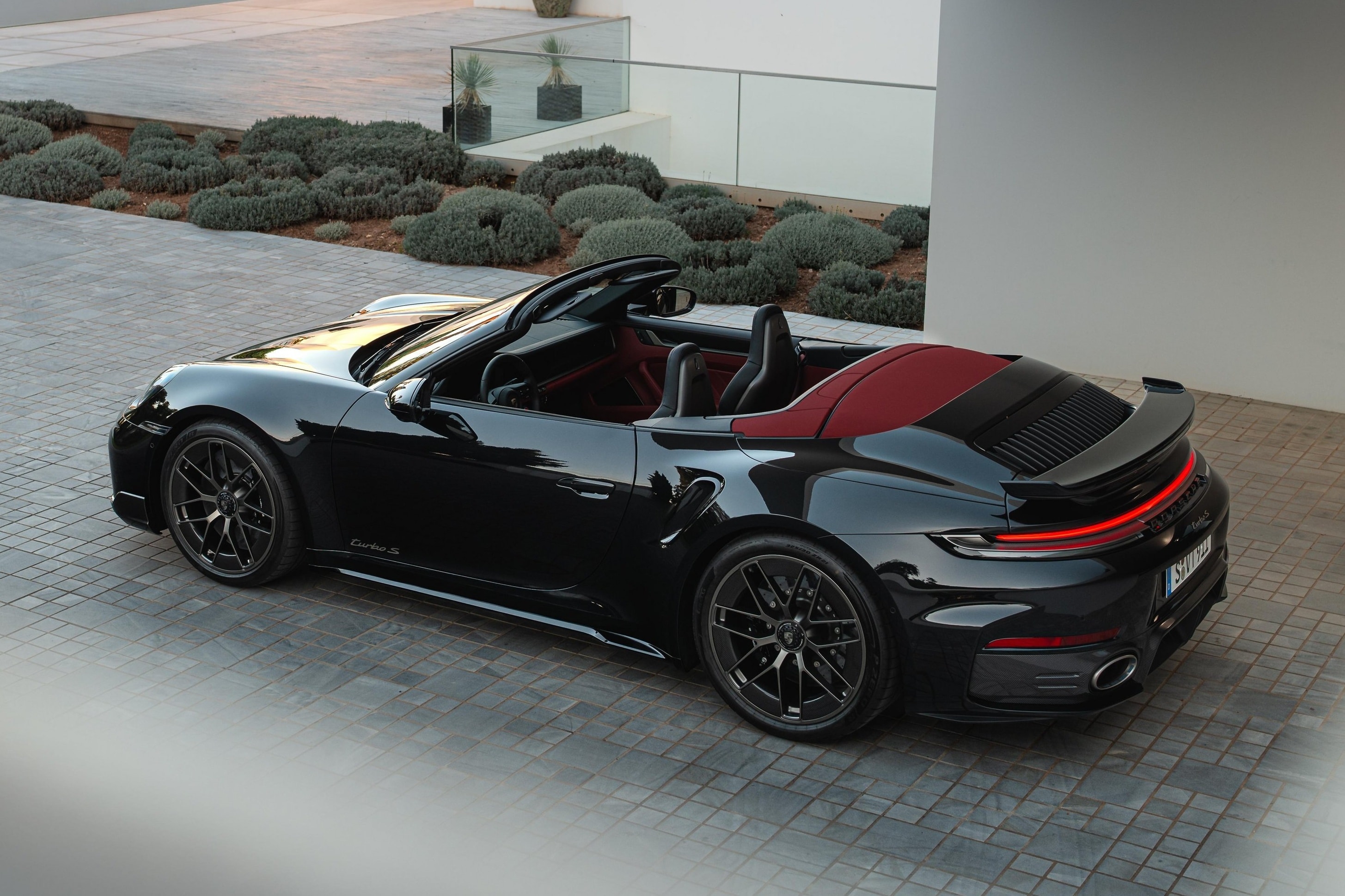 Toàn cảnh Porsche 911 Turbo S Cabriolet 2025 màu xám kim loại với mui đang mở.