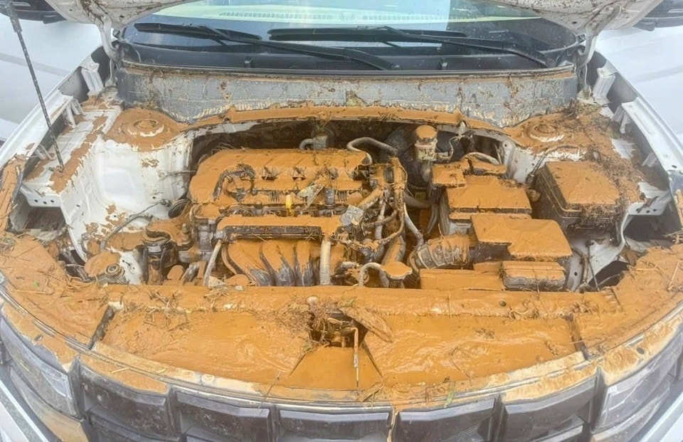 Một chiếc ô tô màu trắng bị bùn đất bao phủ gần hết bánh xe sau khi nước rút.