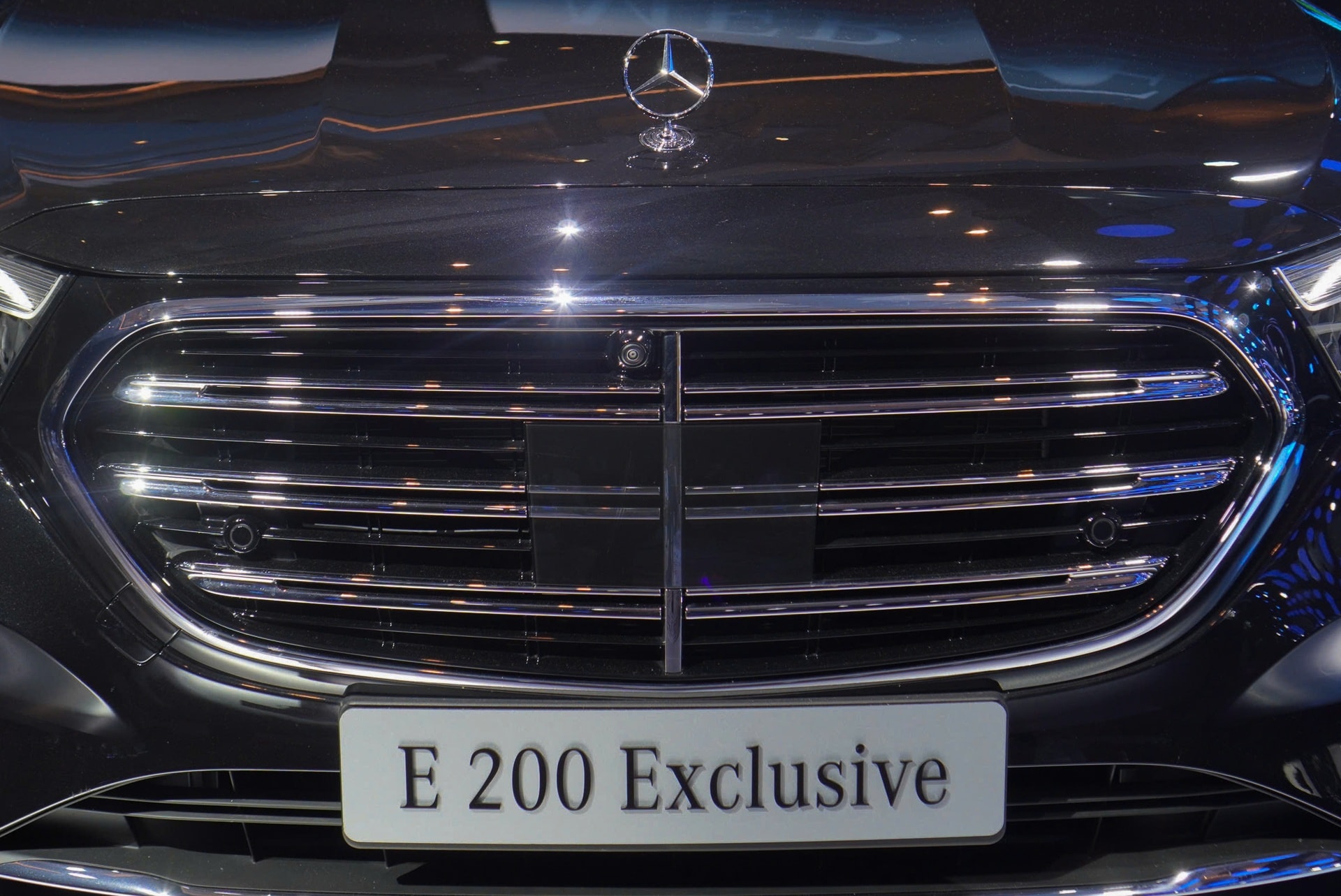 Phần đầu xe Mercedes-Benz E 200 Exclusive với lưới tản nhiệt cổ điển và logo ngôi sao ba cánh trên nắp capo.
