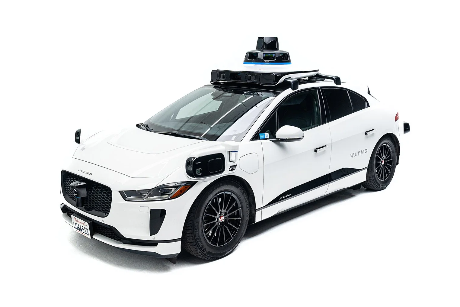 Một chiếc xe tự hành Waymo Jaguar I-Pace màu trắng với cụm cảm biến phức hợp trên nóc xe.