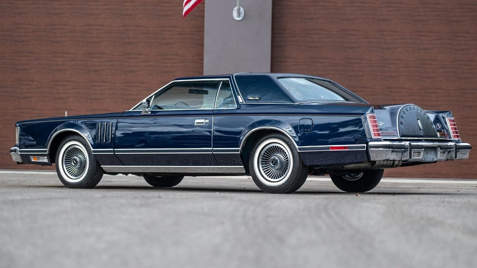 Góc phải phía sau của coupe xanh đậm trước bức tường nâu.