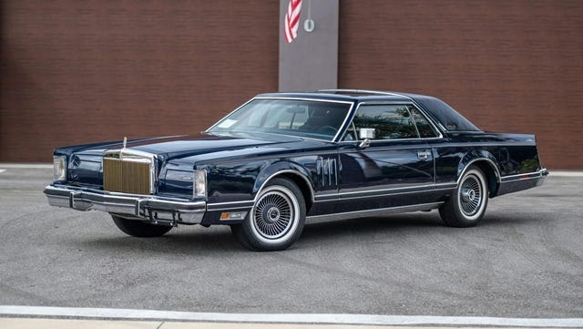 Góc trái phía trước của coupe xanh đậm đỗ trên nền nhựa đường.