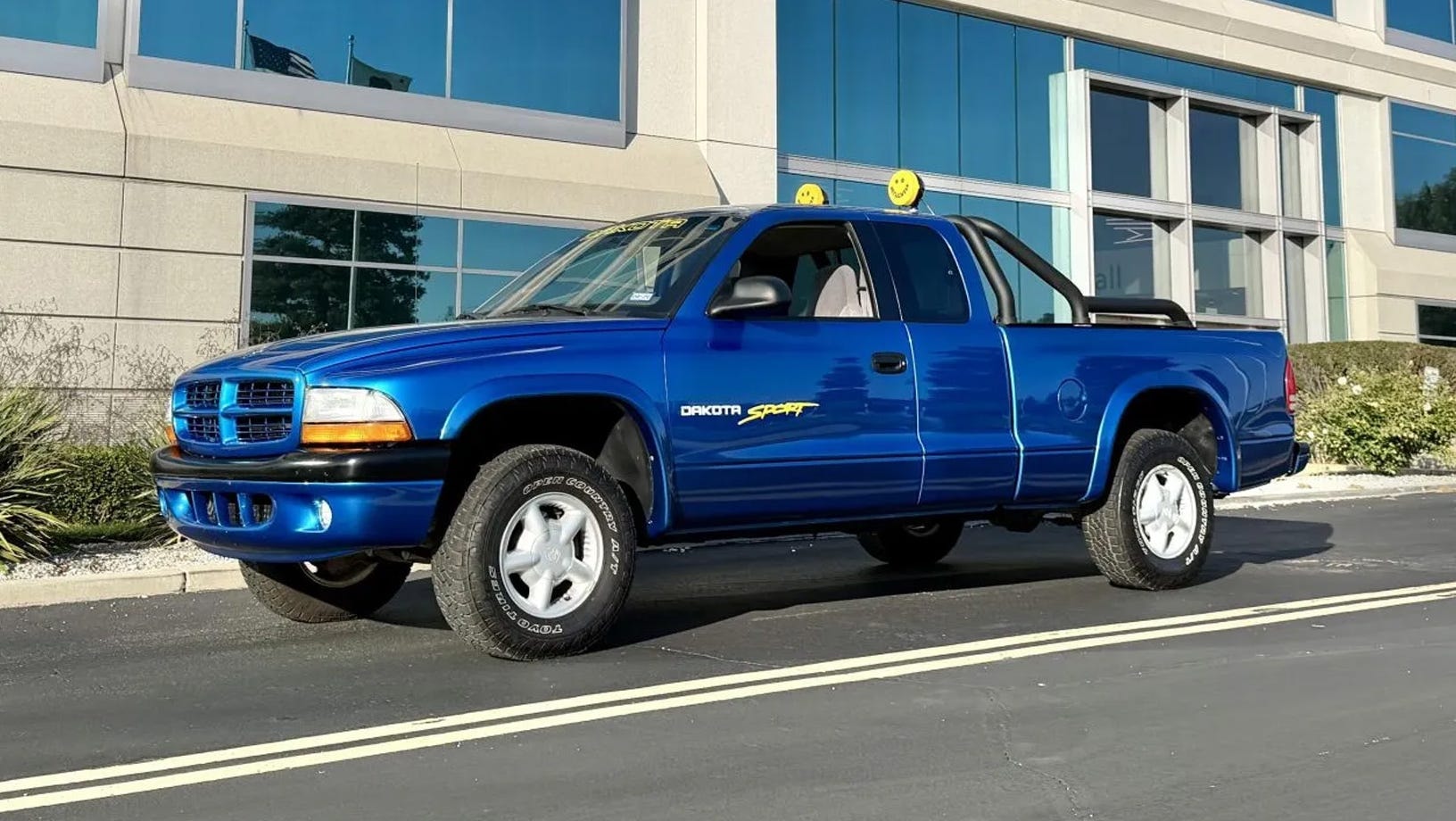 Góc trước trái, bán tải màu xanh đỗ trước tòa nhà kính.