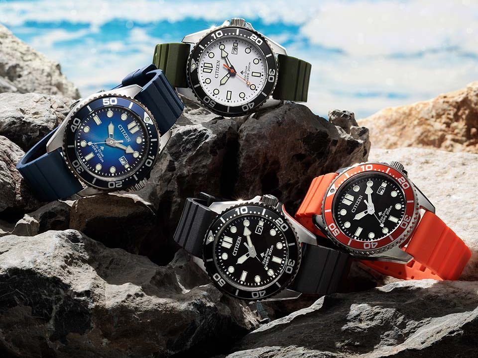 Bốn mẫu đồng hồ lặn Citizen Promaster Marine với các phối màu trắng, đen, xanh dương và cam hiển thị trên đá ven biển.