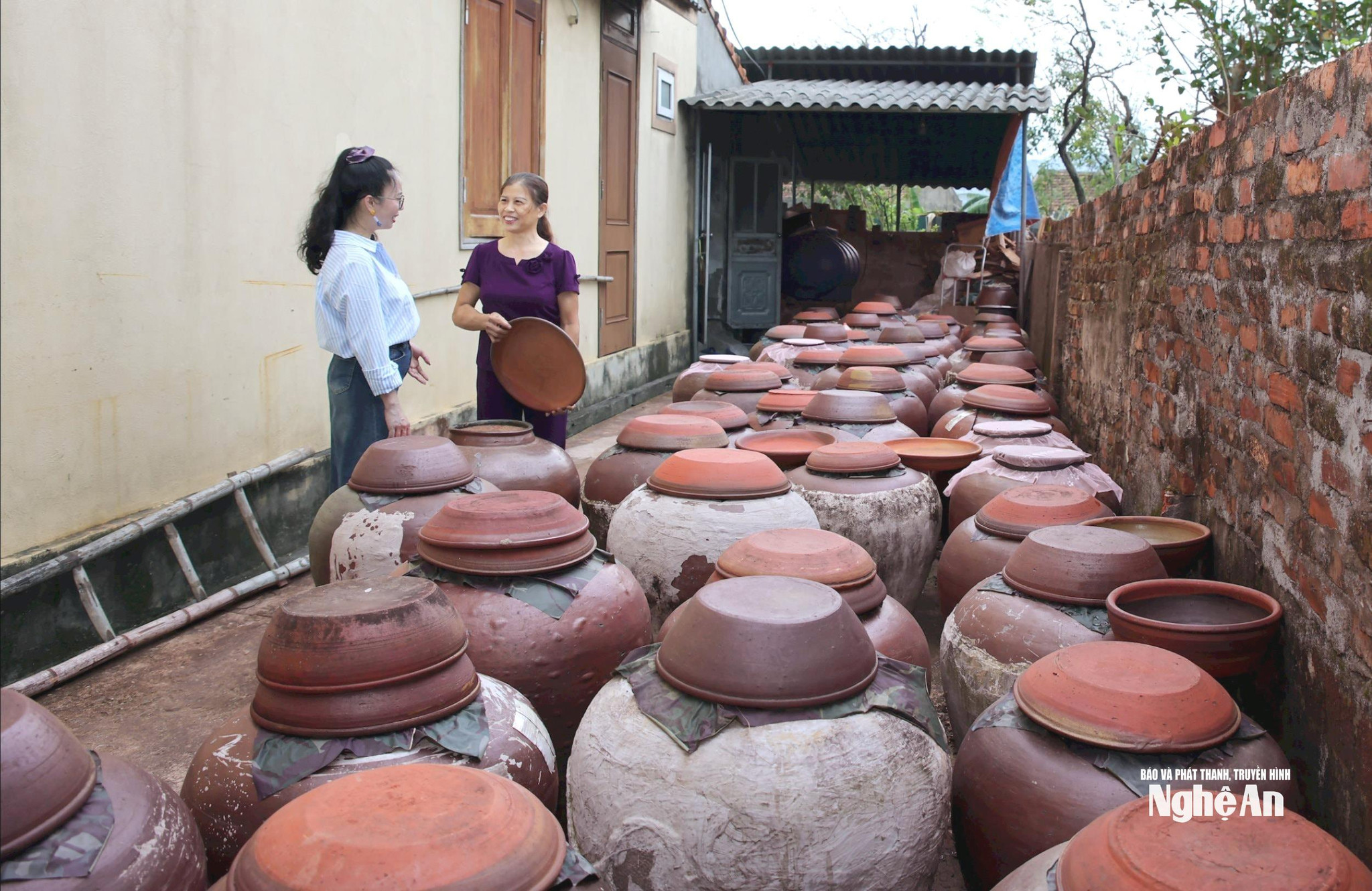 Chị Bùi Thị Hà (SN 1967, bìa phải) ở xóm 4, xã Kim Liên bên cạnh các chum tương của gia đình. Ảnh Thanh Quỳnh